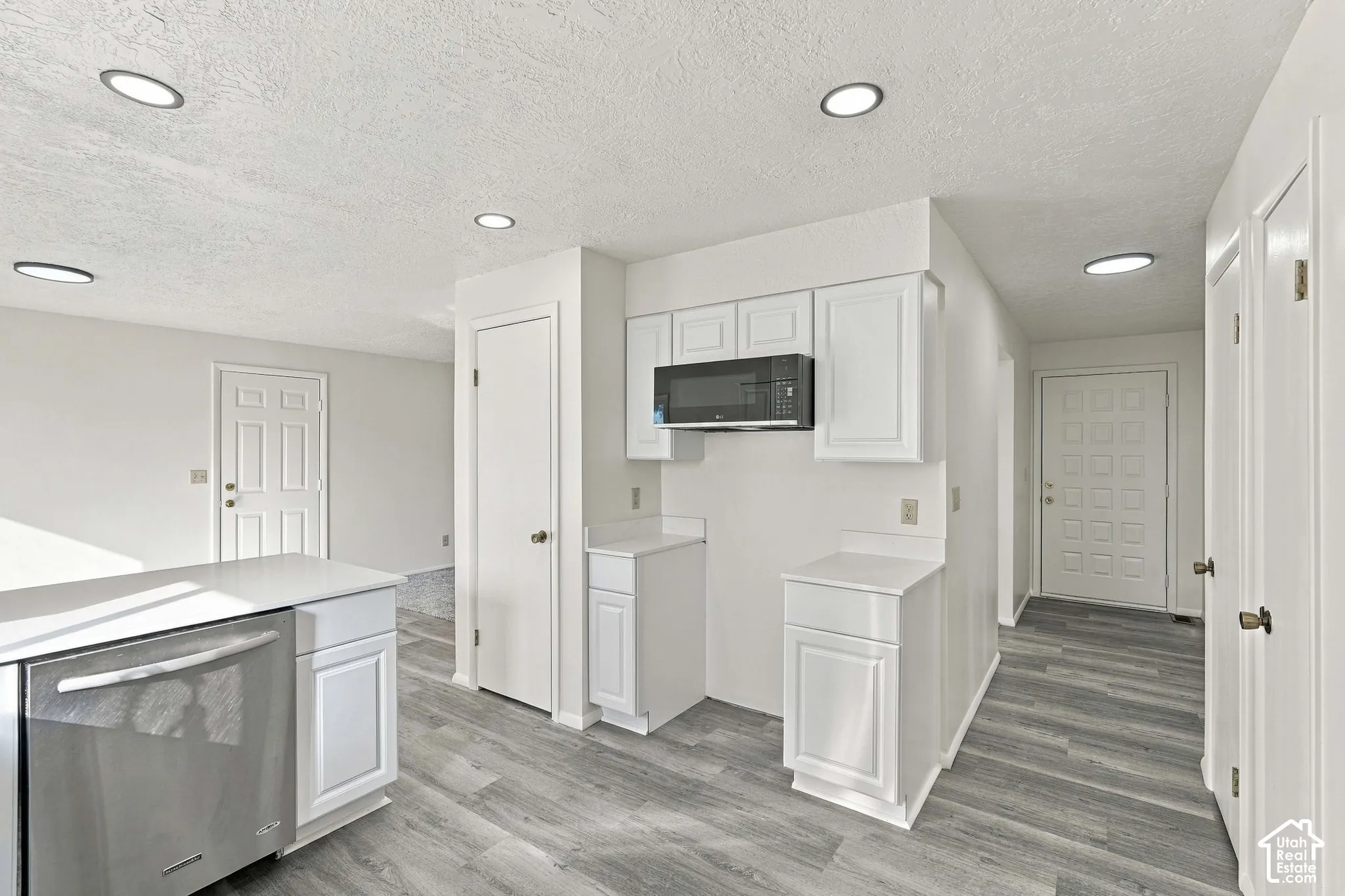 Kitchen featuring wood-finish flooring, white cabinetry, a stainless steel dishwasher, and a built-in microwave