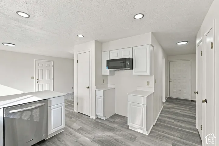 Kitchen featuring wood-finish flooring, white cabinetry, a stainless steel dishwasher, and a built-in microwave