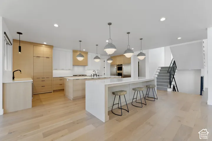 Hardwood flooring, two kitchen islands with solid surface countertops, integrated kitchen appliances, modern pendant lighting, and a staircase with metal railings
