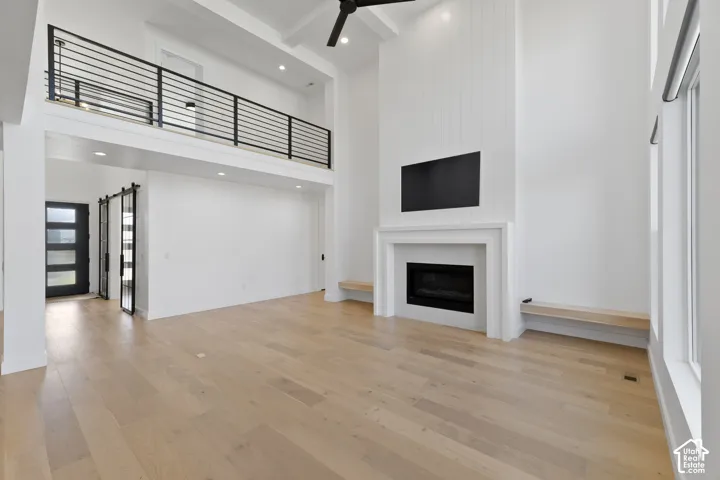 Open-concept living space featuring high ceilings, wood-finish flooring, a contemporary fireplace with a mantel, and a second-story interior balcony with black metal railings