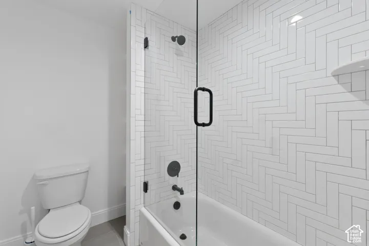 Full glass shower enclosure with matte black hardware, white subway tile in a herringbone pattern, and a built-in shower shelf