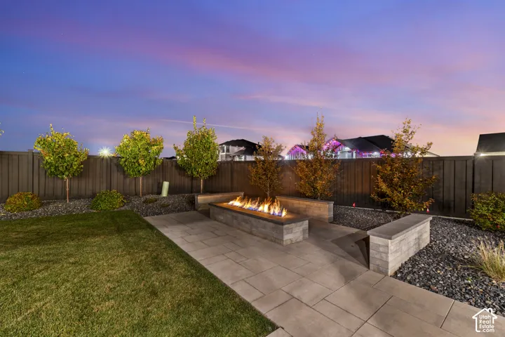 Manicured lawn, paver patio, fire pit feature, stone block retaining walls, and dark-stained fencing
