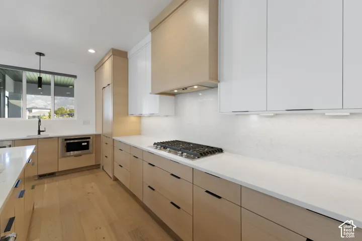 Modern kitchen with light wood-finish cabinetry, white solid-surface countertops, and integrated stainless steel appliances