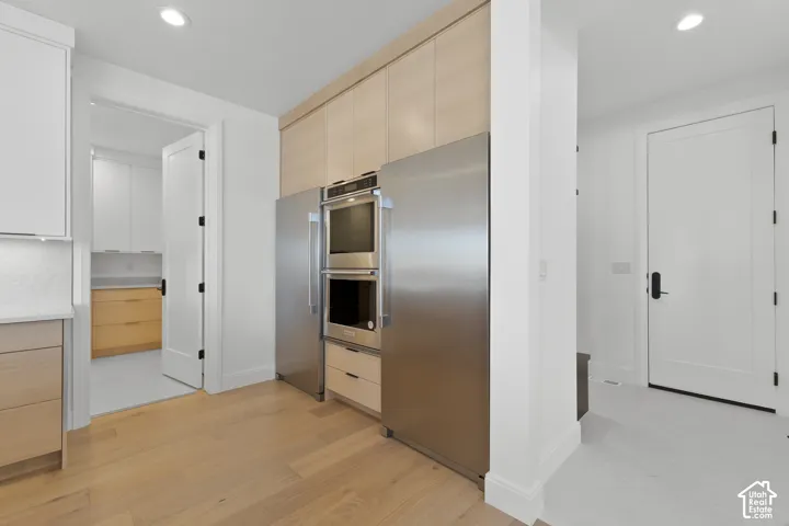 Stainless steel appliances with double ovens, integrated refrigerator, light wood-finish cabinetry, and recessed lighting