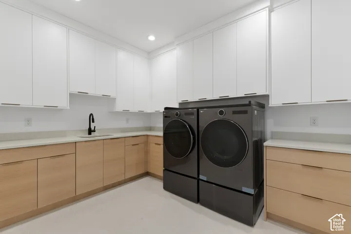 Expansive laundry room featuring white upper cabinetry, wood-finish lower cabinetry, stone countertops, a single basin sink with a matte black faucet, and recessed lighting