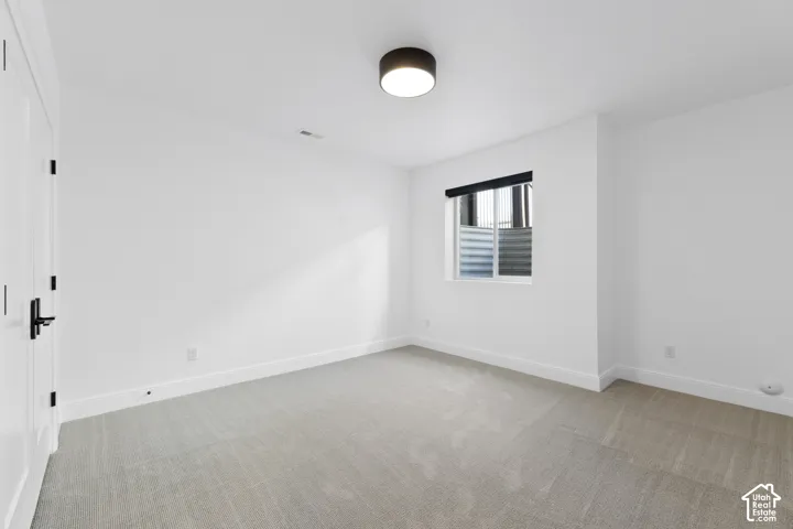 White walls with a single window, featuring a drum ceiling light fixture and light-colored carpeting