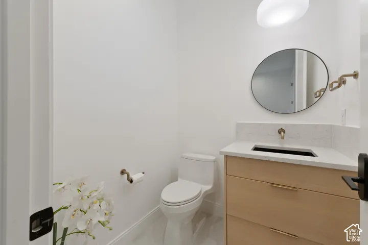 Light wood-finish vanity with integrated sink, stone countertop, matte brass faucet, and circular mirror