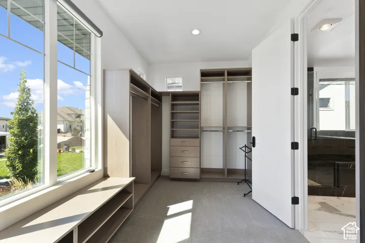Custom closet system with built-in shelving and drawers, window seat with storage, large window, and direct access to a bathroom