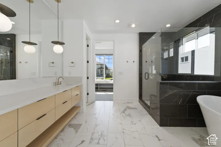 Spacious bathroom featuring a double vanity with wood-finish cabinetry, a large walk-in glass shower, a freestanding bathtub, and white large-format tile flooring