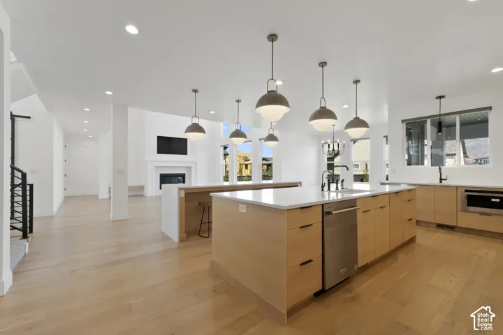 Open-concept kitchen featuring light wood-finish cabinetry, a large island with integrated stainless steel appliances, and pendant lighting