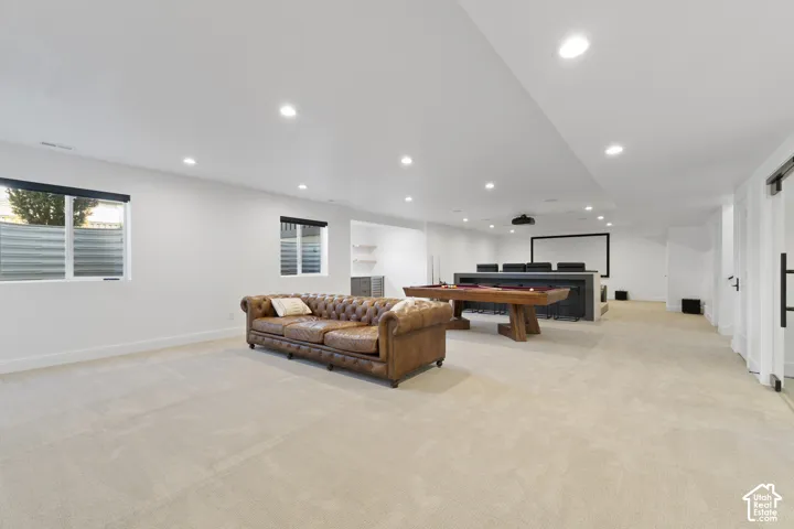 Recessed ceiling lighting, light-toned carpeting, two windows with blinds, a built-in media center, and white walls