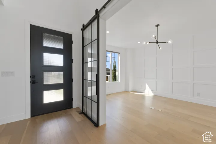 White walls with decorative wainscoting, wood-finish flooring, and a modern chandelier