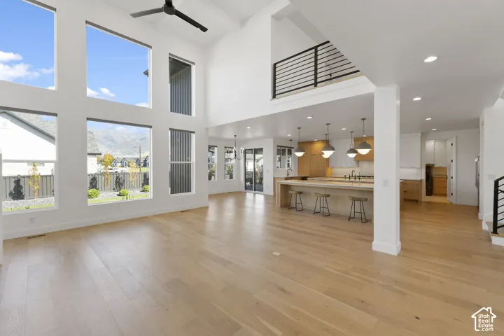 Expansive living area with high ceilings, large multi-pane windows, wood-finish flooring, and a modern kitchen featuring a central island with pendant lighting