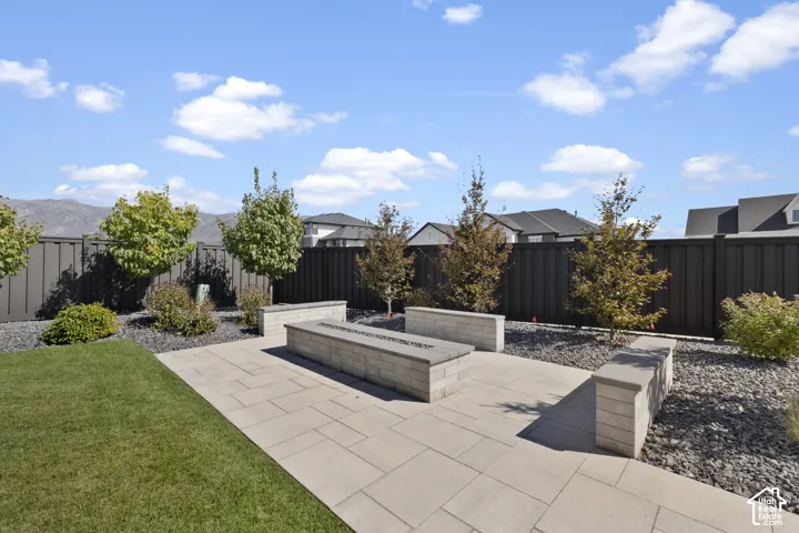 Expansive backyard oasis featuring a manicured lawn, modern concrete hardscape with integrated planter boxes, mature landscaping with trees and shrubs, decorative gravel accents, and black aluminum fencing