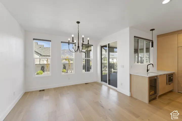 Wide plank wood-finish flooring, multiple windows, sliding glass door, modern chandelier, and a built-in wet bar with a beverage cooler