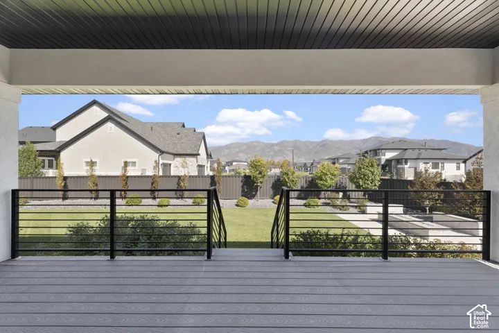 Covered porch with composite decking and black horizontal bar railing overlooking a manicured lawn and mountain scenery