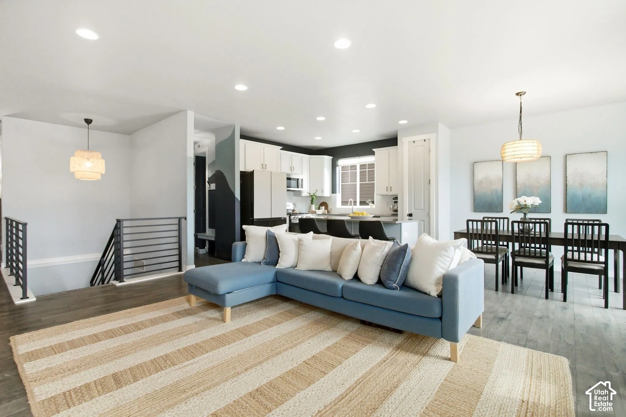 Open-concept living area with wood-finish flooring, recessed lighting, and a modern horizontal metal railing system