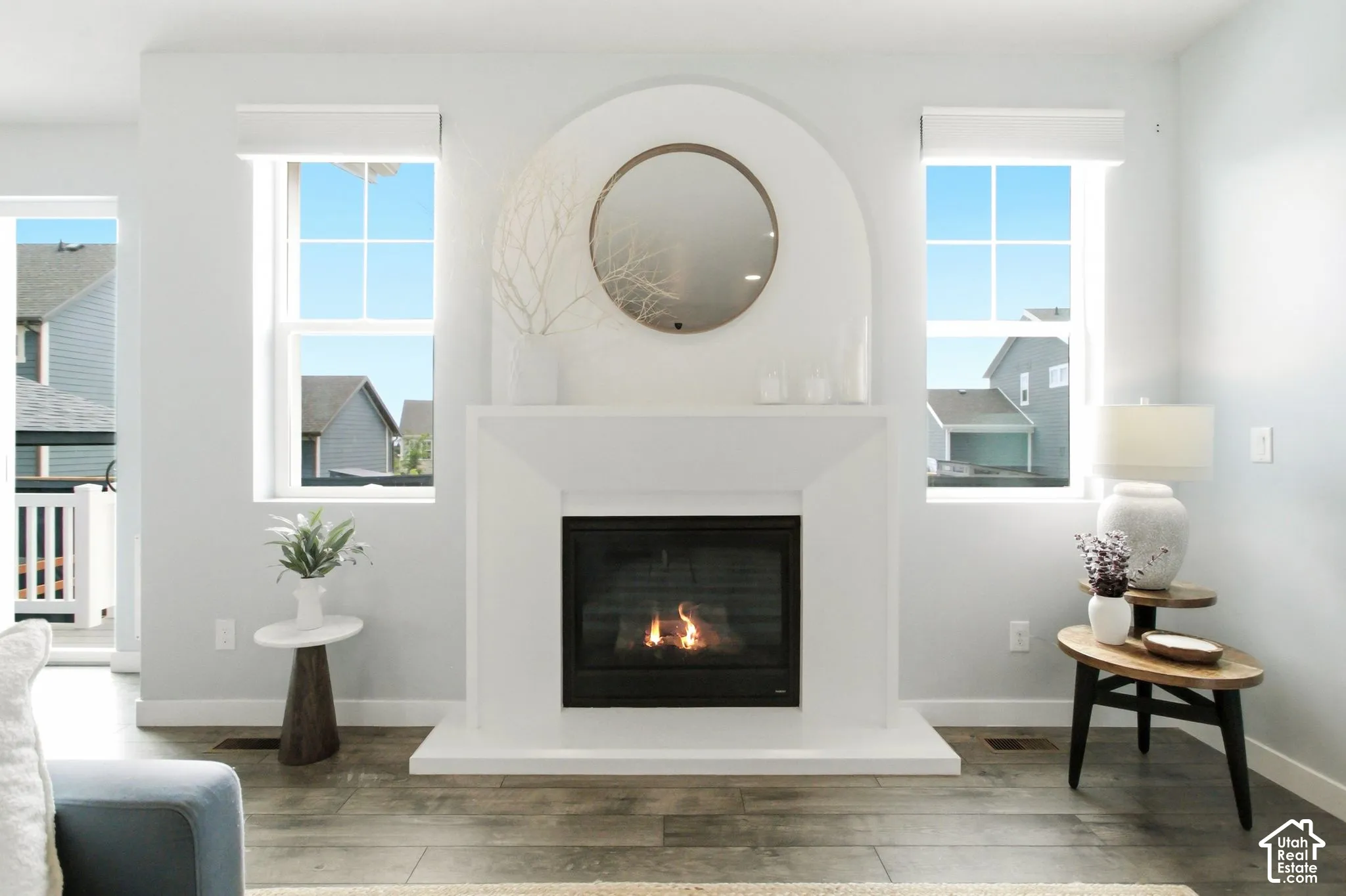 Fireplace with an arched mantel, wood-finish flooring, and multiple windows with roller shades