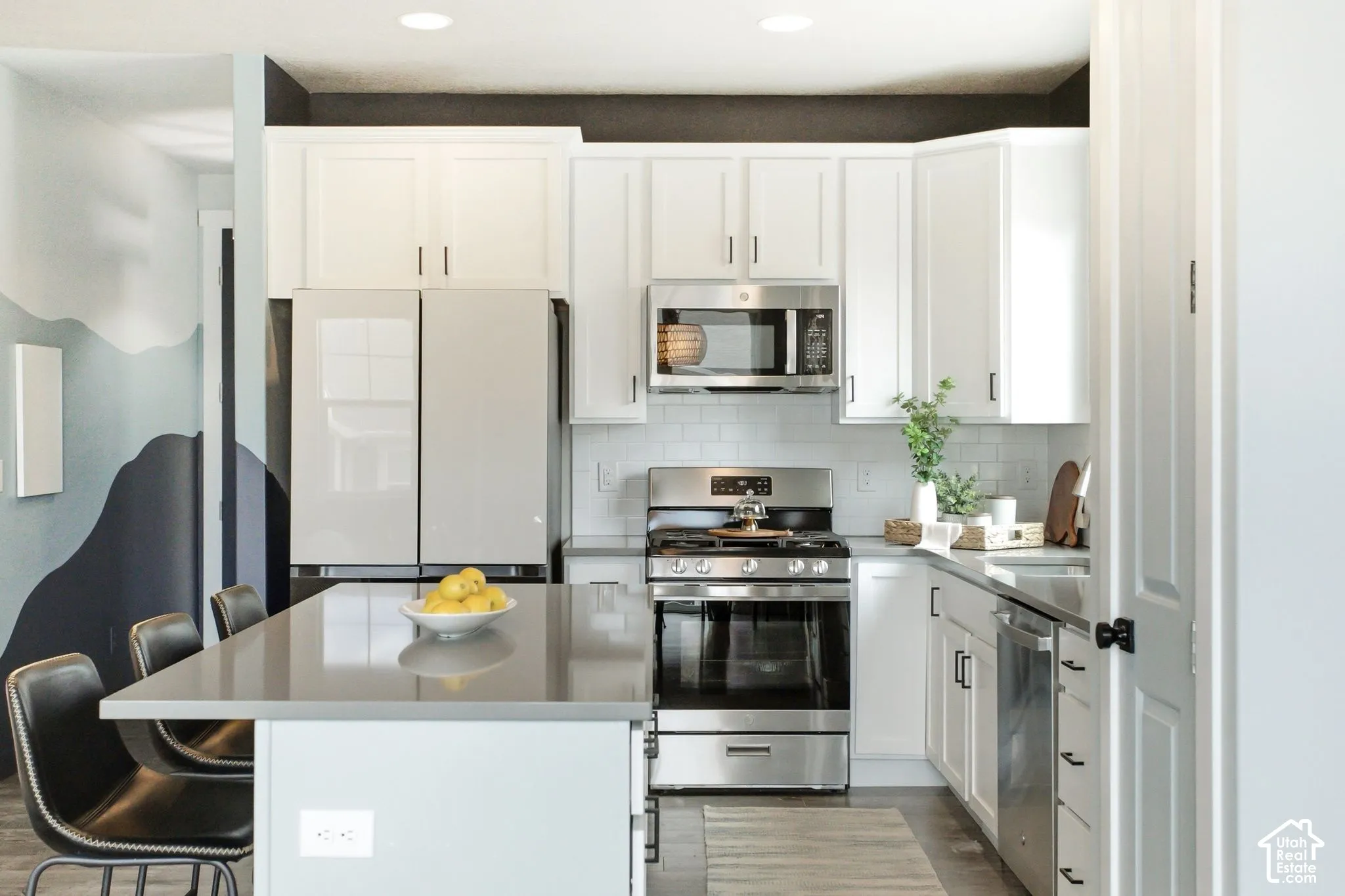 Modern kitchen featuring white cabinetry, stainless steel appliances, a subway tile backsplash, a kitchen island with seating, and wood-finish flooring