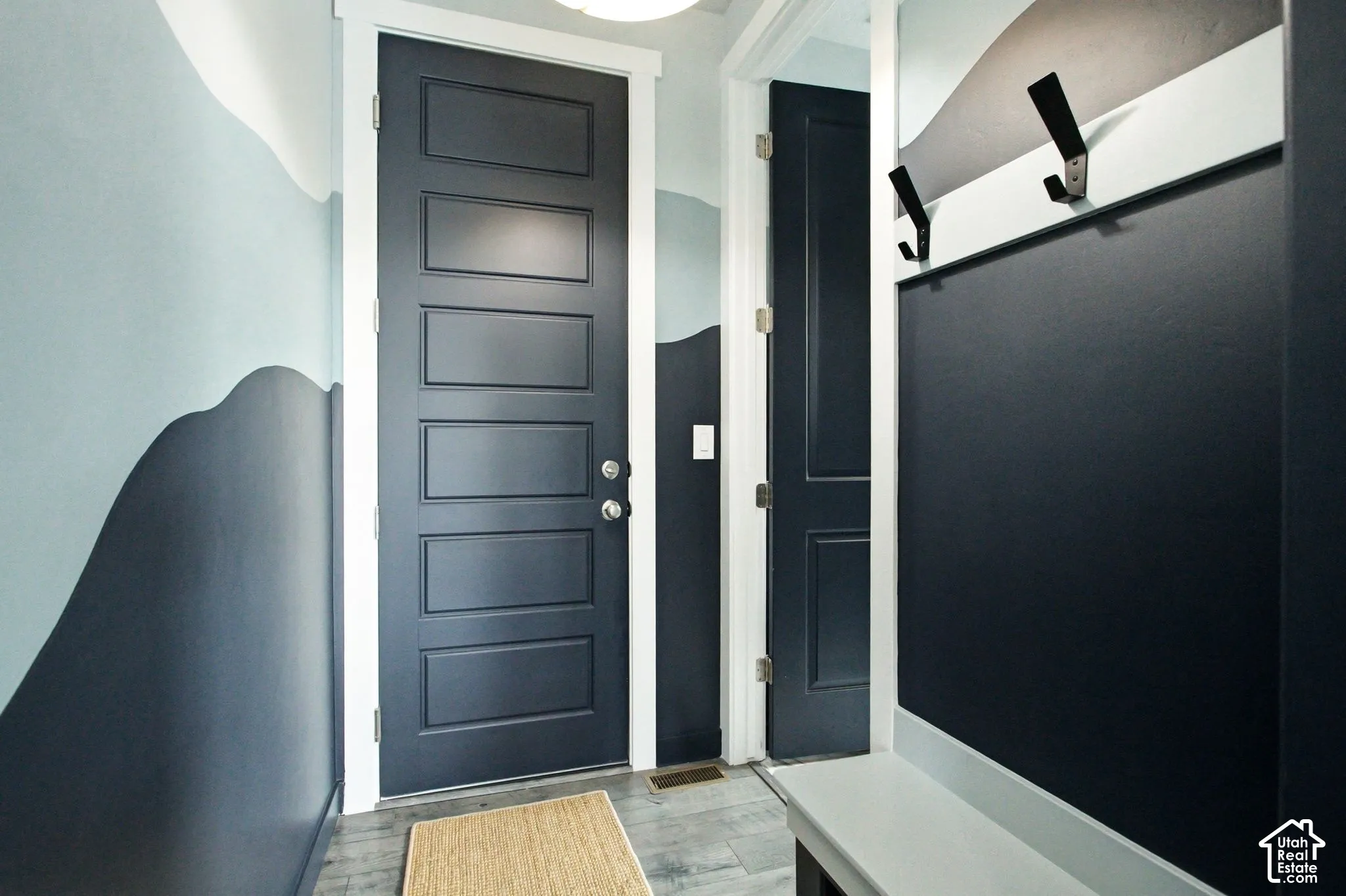 Painted accent wall, five-panel entry door, dark wood-finish flooring, built-in coat hooks, and integrated bench seating