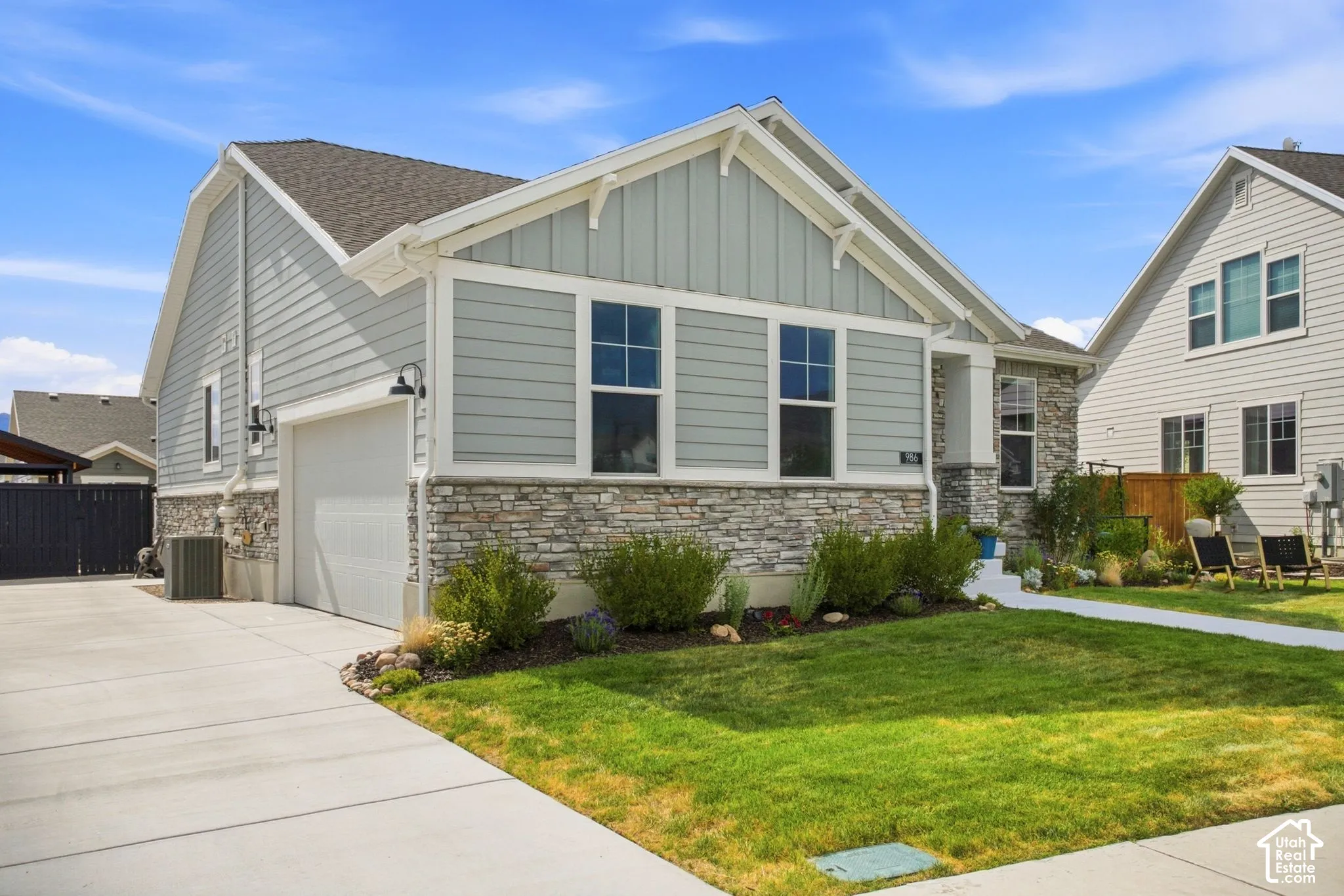 Light gray siding exterior with stone veneer accents, an attached garage, landscaped front yard, and a concrete driveway