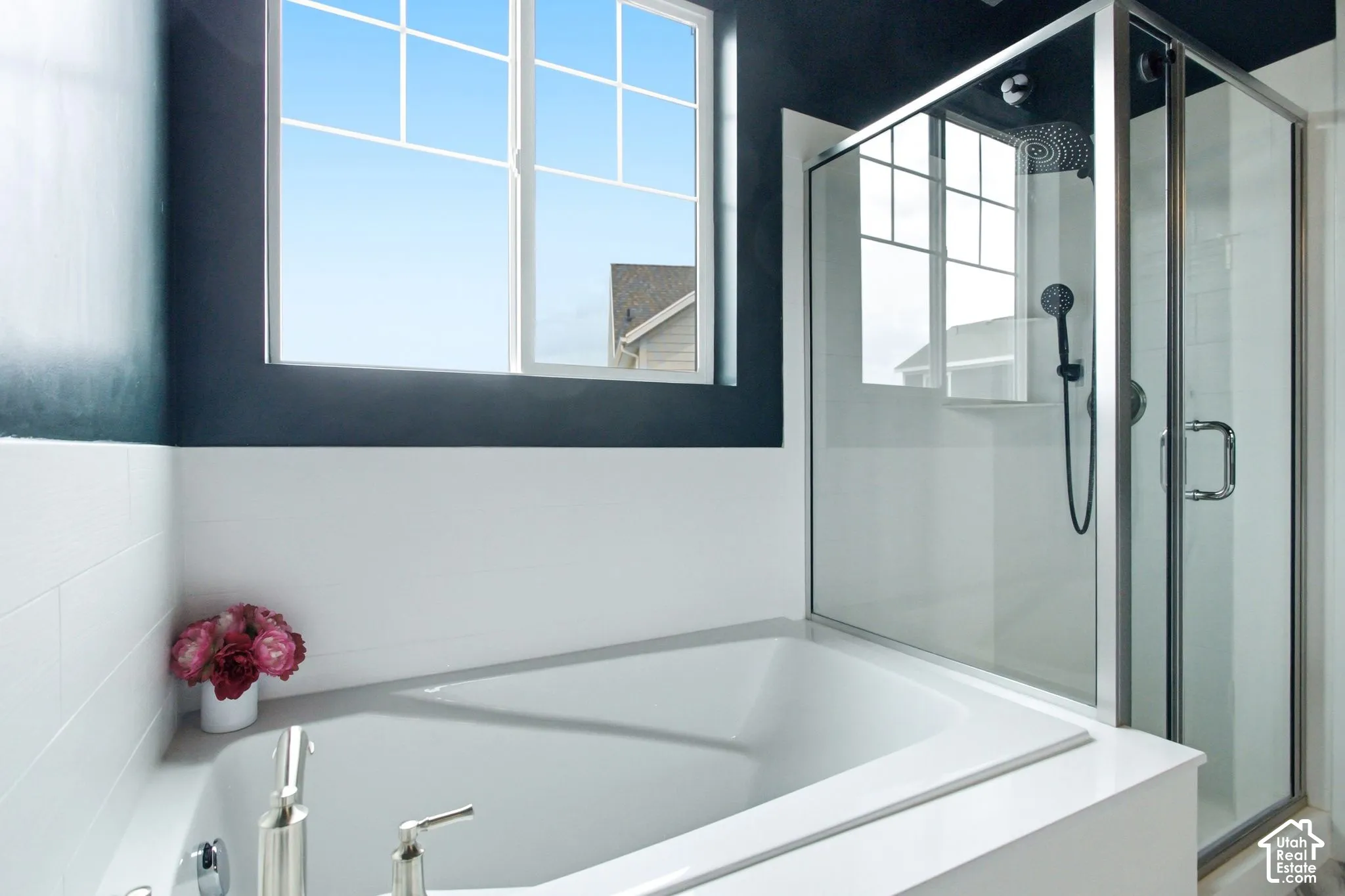 Built-in soaking tub with polished chrome fixtures, glass-enclosed shower with a rainfall showerhead, and a grid-pattern window