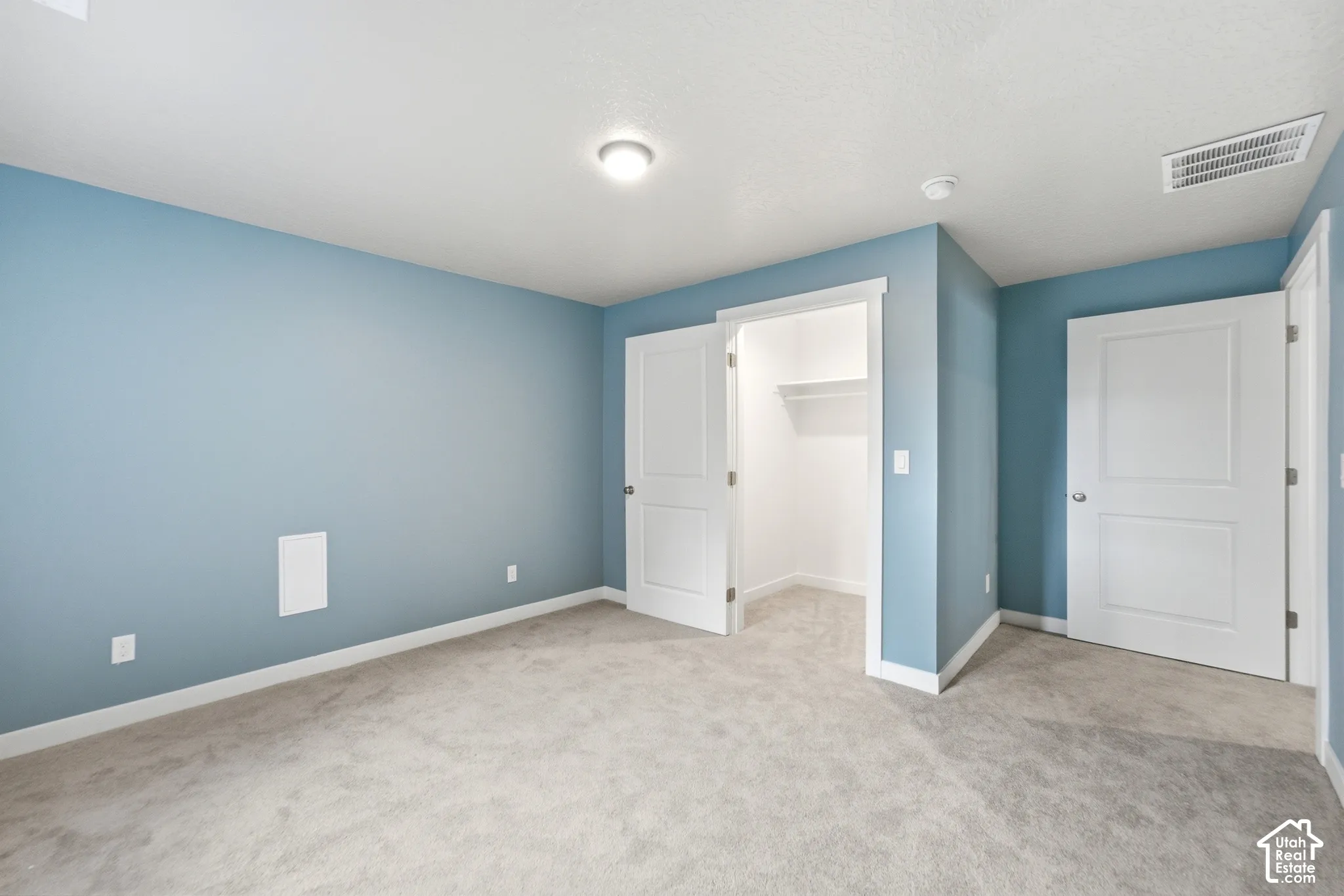 Spacious bedroom featuring soft blue-painted walls, neutral carpet flooring, recessed ceiling lighting, and dual white six-panel closet doors providing ample storage