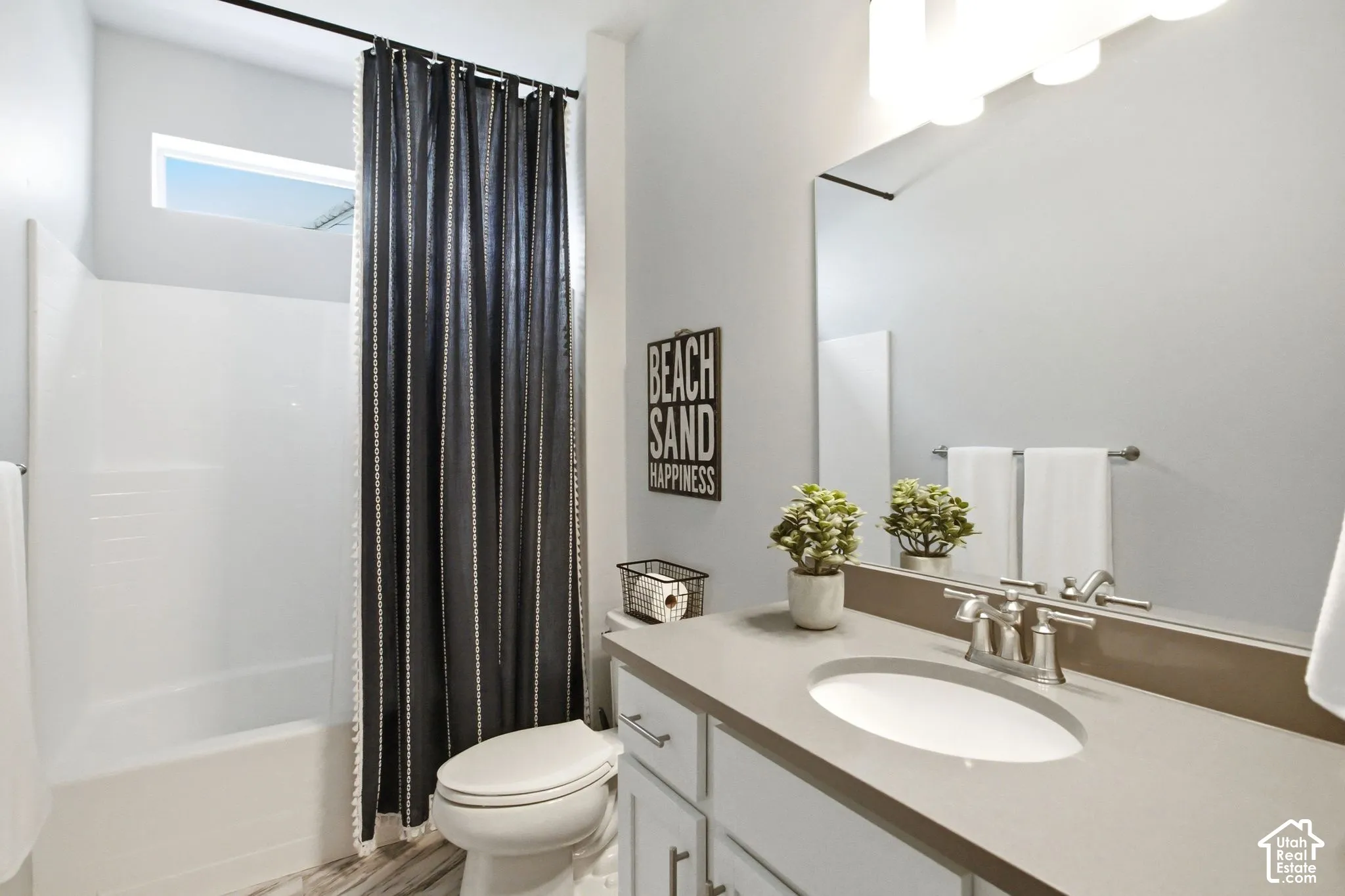 Modern vanity with an integrated sink and brushed nickel faucet, full-width mirror, and a white bathtub with an overhead window