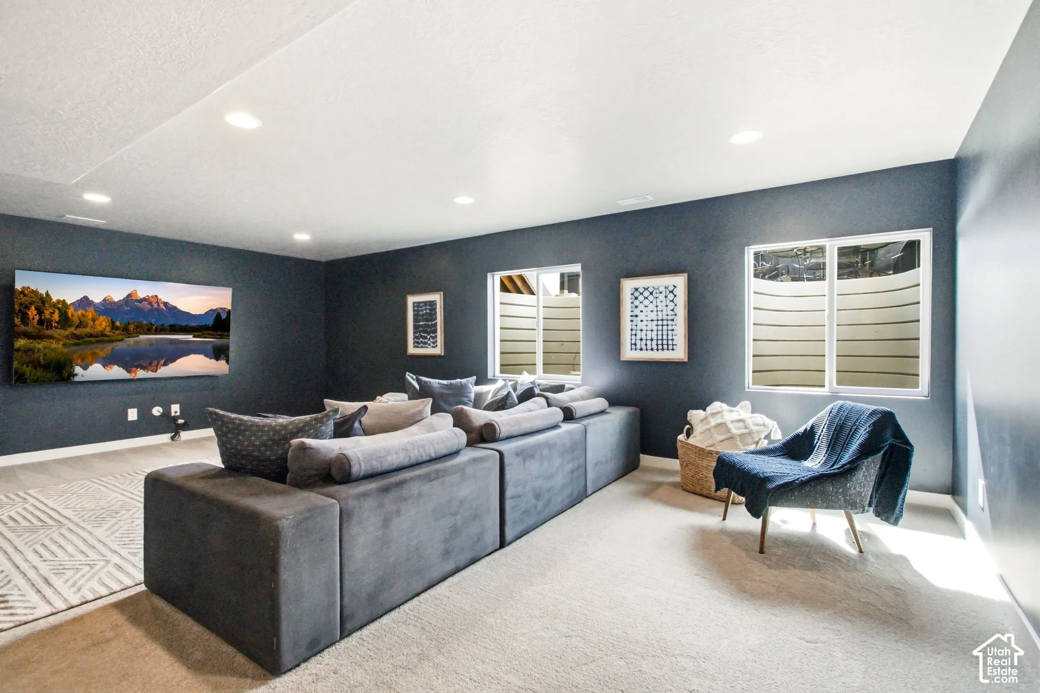 Recessed ceiling lighting, two windows with white frames, dark-colored walls, and light-colored carpet flooring