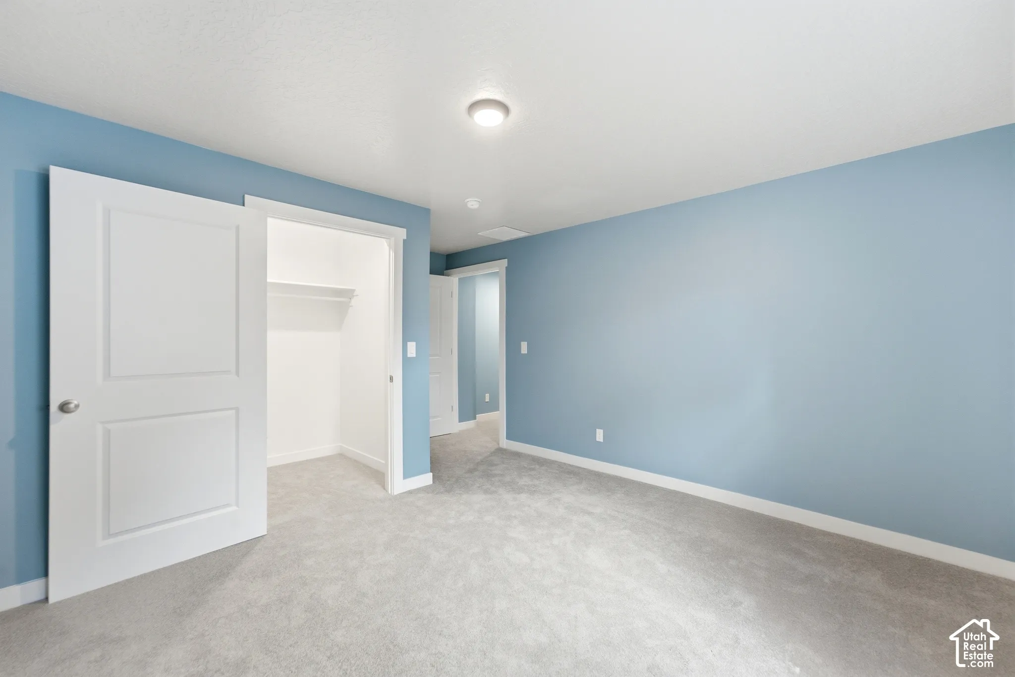 Plush carpet flooring, light blue wall finishes, white trim, recessed lighting, and a closet with shelving and hanging rod