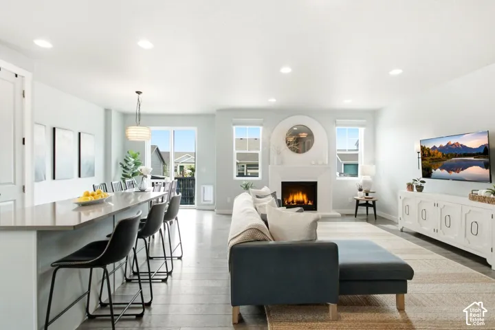 Open-concept living area with wood-finish flooring, a contemporary fireplace, recessed lighting, and a kitchen island with seating
