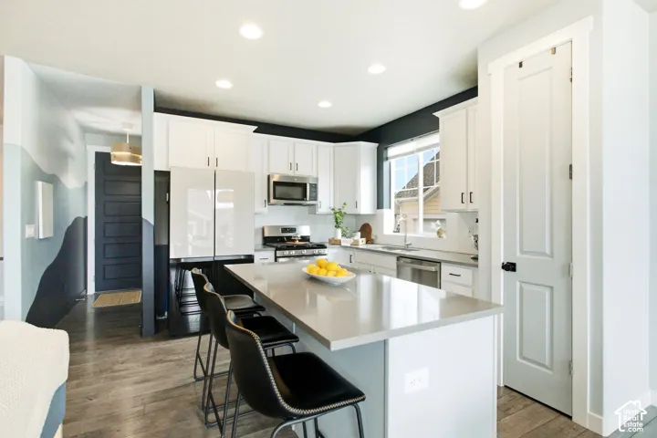 Kitchen featuring white cabinetry, stainless steel appliances, a light-toned countertop island, wood-finish flooring, and recessed lighting