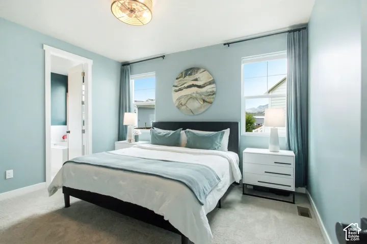 Carpeted flooring, two windows with curtain rods, light blue wall paint, and a built-in overhead light fixture