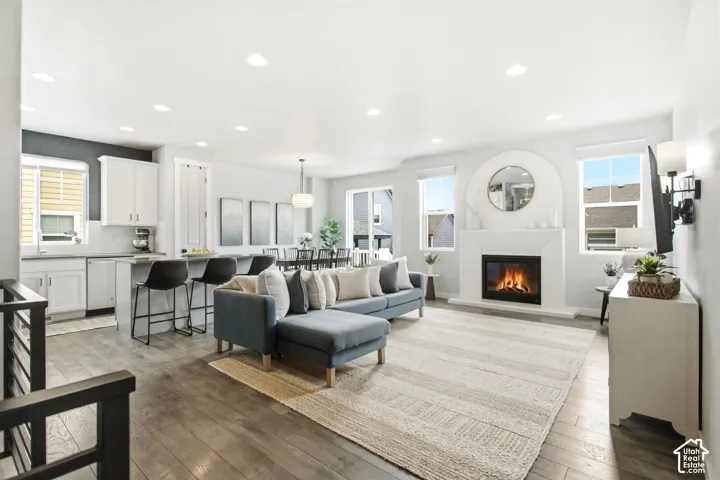 Open-concept living area featuring wood-finish flooring, a contemporary fireplace, recessed lighting, and white cabinetry