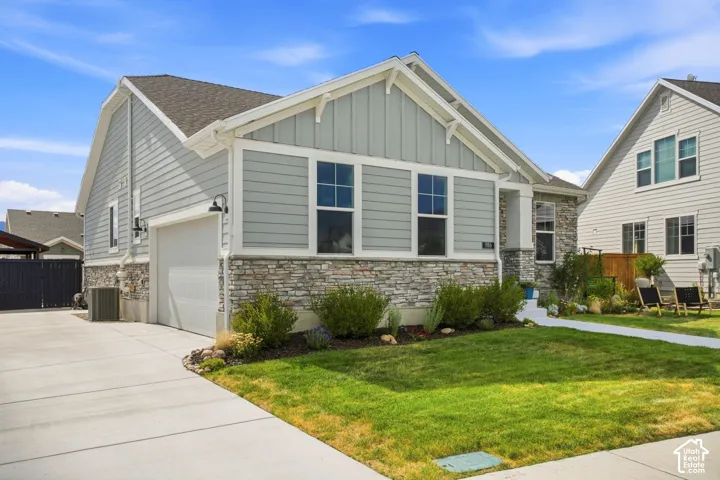 Light gray siding exterior with stone veneer accents, an attached garage, landscaped front yard, and a concrete driveway