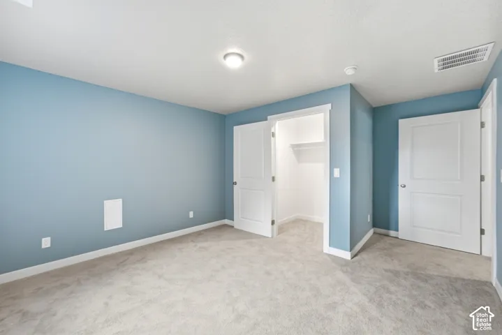 Spacious bedroom featuring soft blue-painted walls, neutral carpet flooring, recessed ceiling lighting, and dual white six-panel closet doors providing ample storage