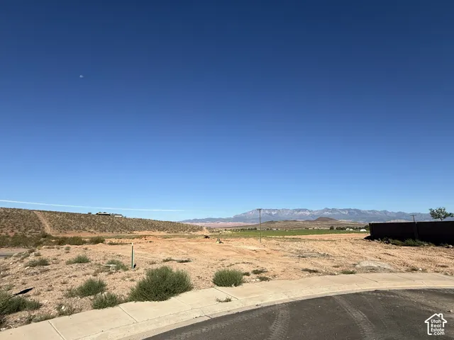 Expansive undeveloped land featuring a paved road, concrete sidewalk, and mountain scenery