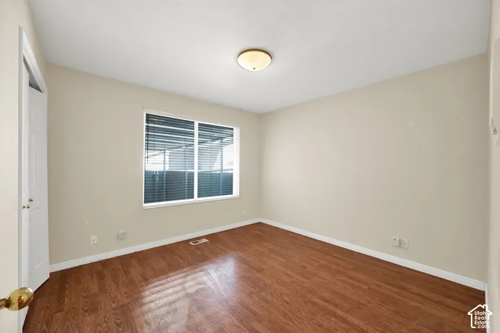 Wood-finish flooring with a large window featuring horizontal blinds, and a ceiling-mounted light fixture