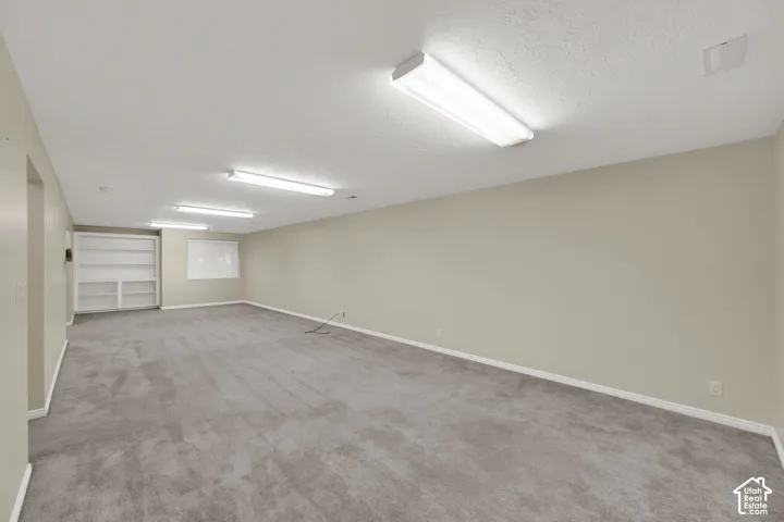 Expansive carpeted room featuring built-in shelving, neutral wall tones, and overhead fluorescent lighting