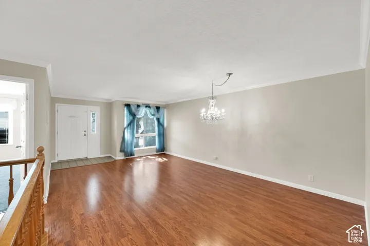 Wood-finish flooring, crown molding, white trim, and a crystal chandelier