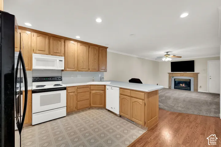 Open-concept kitchen and living area featuring wood cabinetry, stainless steel appliances, a large center island with white countertop, wood-finish flooring, and a gas fireplace with wood mantel in the adjacent living space