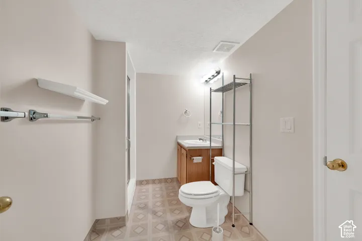 Spacious bathroom featuring a wood-finish vanity with integrated sink, ceramic tile flooring in a geometric pattern, white ceramic toilet, glass-enclosed shower enclosure with metal framing, and abundant natural lighting from recessed ceiling fixtures