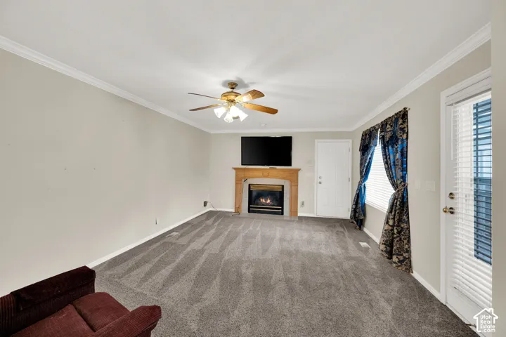 Living area featuring a gas fireplace with a wood mantel, crown molding, and a ceiling fan