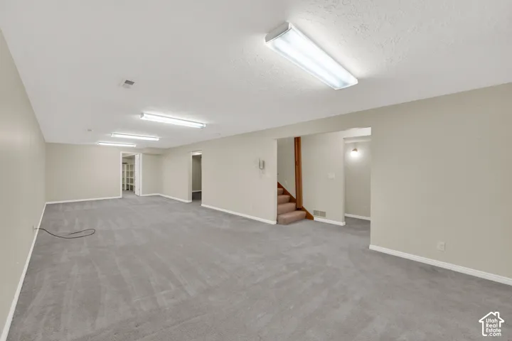 Expansive room featuring gray carpet flooring, light neutral-toned walls, and recessed fluorescent lighting