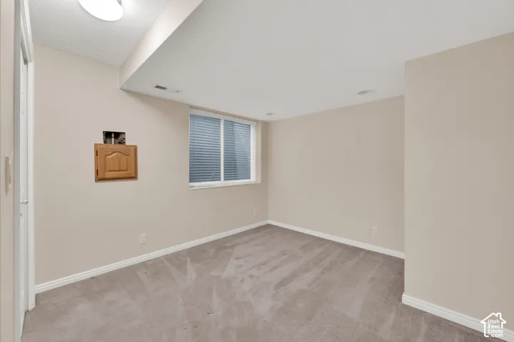 Neutral tone wall paint, light-colored carpeting, a single window with horizontal blinds, and a wood-finish cabinet with an arched panel