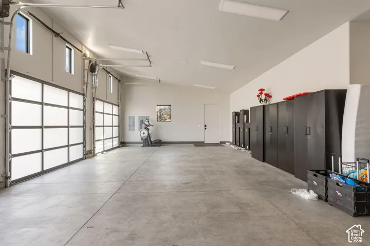 Spacious garage featuring two translucent panel overhead doors, concrete flooring, multiple ceiling-mounted light fixtures, and high-set windows
