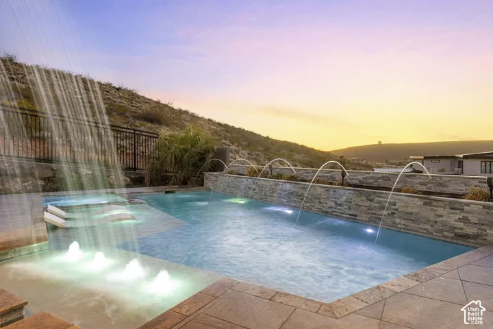 Swimming pool featuring multiple water features, integrated lighting, and surrounding natural rock landscaping