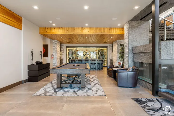 Stone accent walls, wood-paneled ceiling, built-in bar, glass-enclosed wine storage, and a modern fireplace