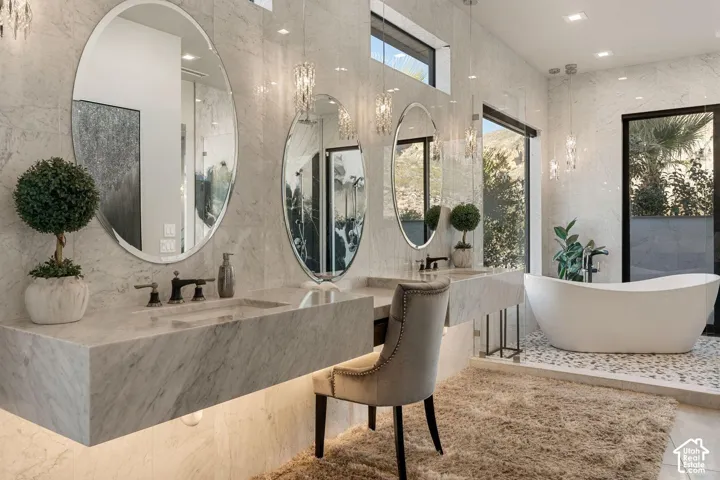 Dual floating vanity with integrated sinks, contemporary oval mirrors, pendant lighting, freestanding soaking tub, and large format wall tile