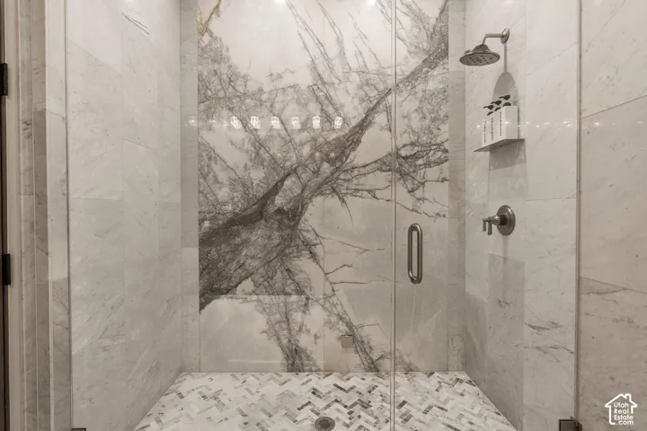 Glass-enclosed shower featuring a striking veined stone accent wall, herringbone mosaic tile floor, and a built-in shower niche